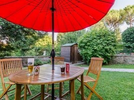 Una mesa de madera con cuatro sillas, un paraguas rojo y dos vasos de cerveza.