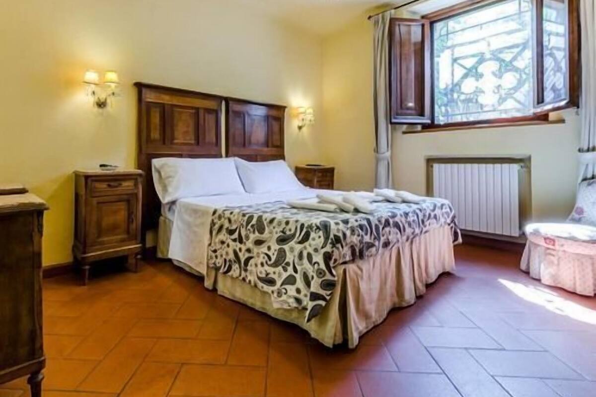 A bedroom with a wooden bed, two bedside tables, a radiator, and a window with curtains.