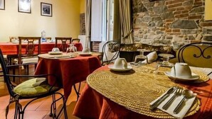 A dining area with a stone wall, red tablecloths, and metal chairs. - Sangaggio House B&B (Florence)