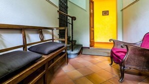 A hallway with a wooden bench and a wicker chair, a tiled floor, and a door leading to a room with a yellow wall. - Sangaggio House B&B (Florence)