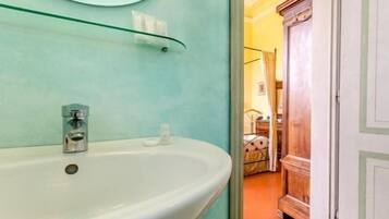 Ein Badezimmer mit einem weißen Waschbecken, einem Glasregal darüber und einem Spiegel an der Wand.
