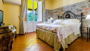 A bedroom with a double bed, a bedside table with a lamp, a window with curtains, a stone wall, and a wooden dresser. - Sangaggio House B&B (Florence)