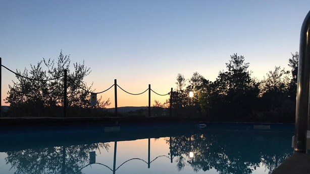 A tranquil outdoor pool area with a clear view of the sunset, surrounded by trees and a fence. - Il Pettirosso di Siena (Siena)