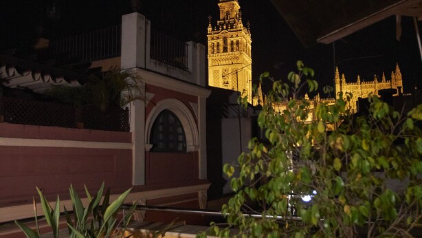 A night view of a building with a prominent tower, potted plants, and a balcony. - U-Sense Sevilla Centro (Seville)