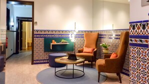 A lobby with a patterned tile wall, a round coffee table with a laptop, and two armchairs. - U-Sense Sevilla Centro (Seville)