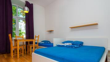 Un dormitorio con dos camas, una mesa de madera, sillas, un ventanal con cortinas y una lámpara colgante.
