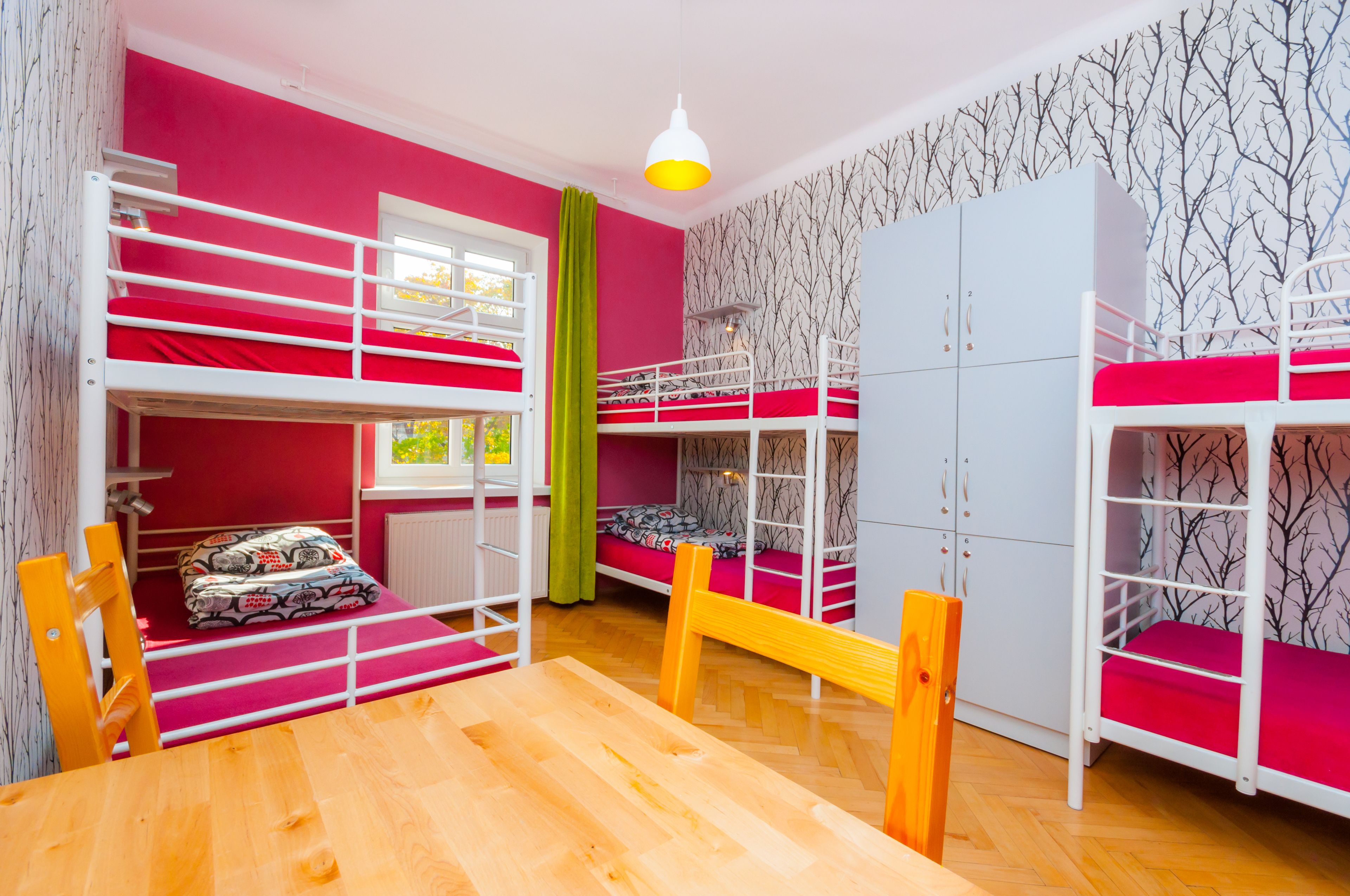 Una habitación con literas, una mesa de madera y un ventanal con cortinas.