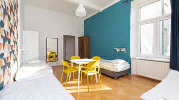 Una habitación con dos camas, una mesa de comedor con sillas amarillas, una ventana con cortinas y una pared de acento azul.