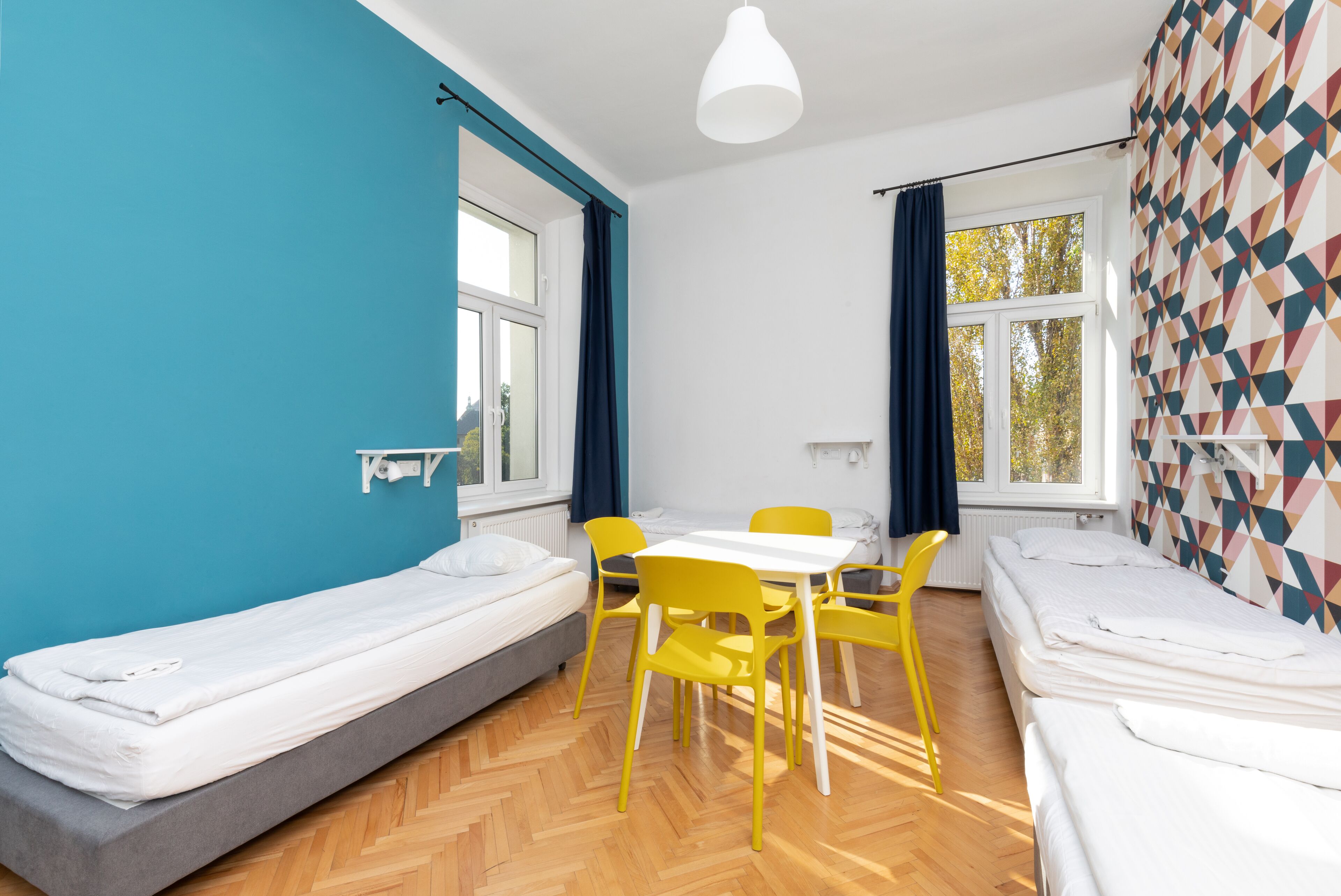 A room with two single beds, a small table with chairs, and a window with curtains.