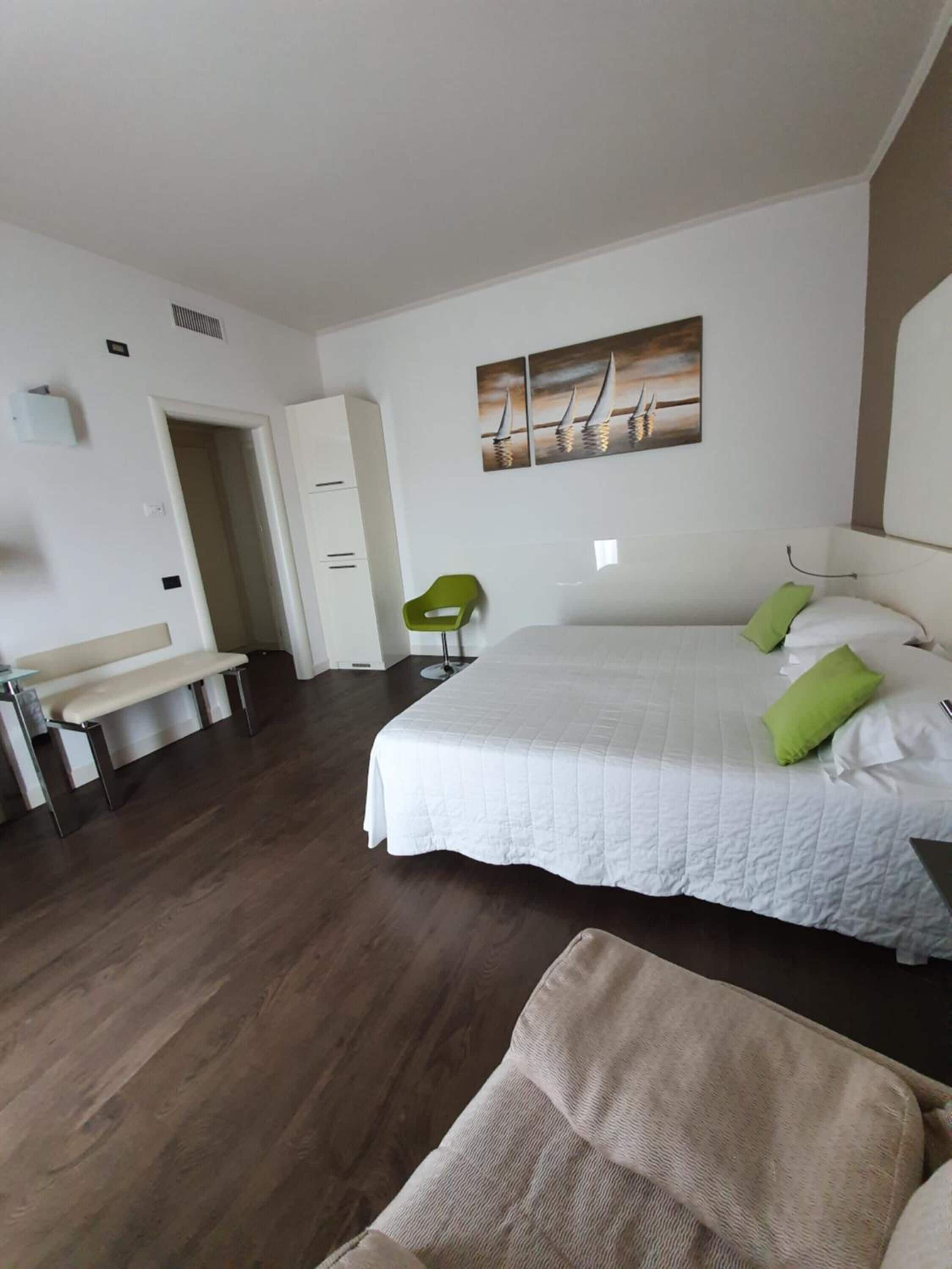Habitación de hotel con una cama grande, un banco, una silla y un cuadro en la pared.