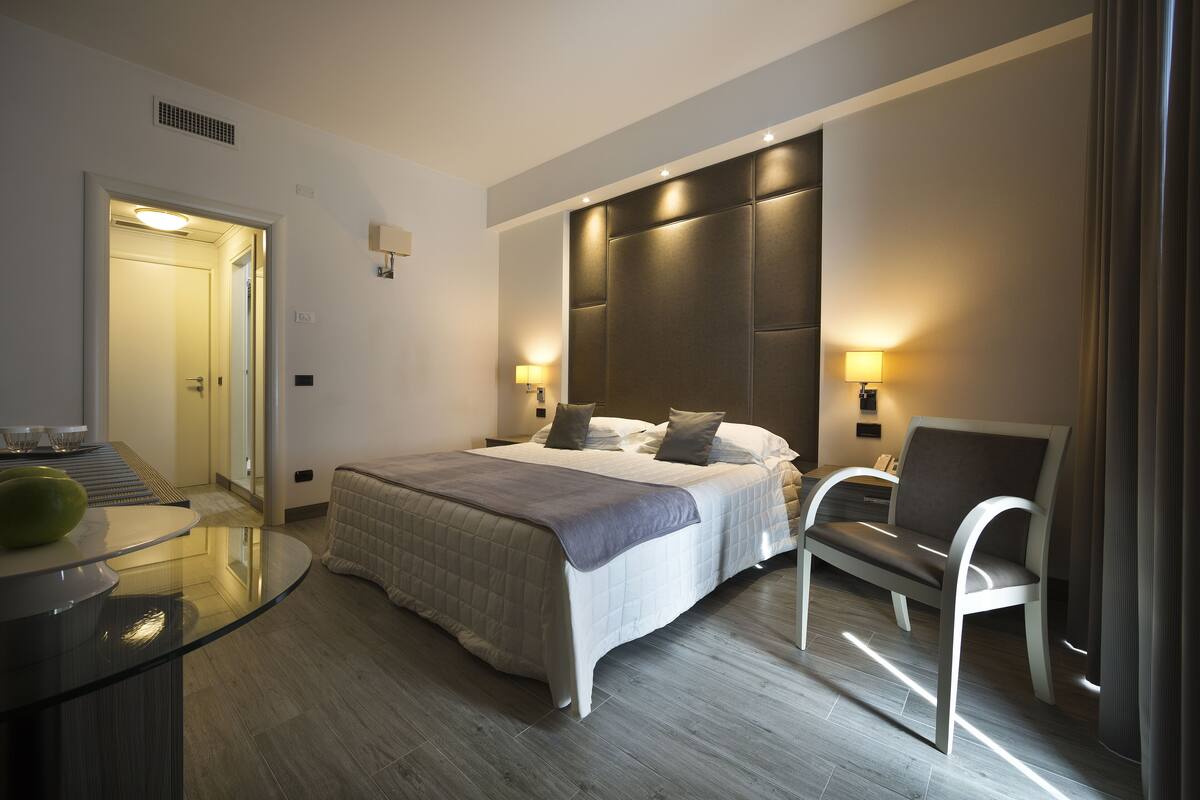 Une chambre d’hôtel moderne avec un grand lit, des lampes de chevet, une table en verre et un coin salon.