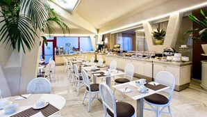 Un espace de restauration moderne, avec des meubles blancs, un buffet et une vue sur l’entrée de l’hôtel.