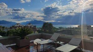 Une terrasse sur le toit, dotée de chaises longues et d’une table, offrant une vue sur un plan d’eau et des montagnes.