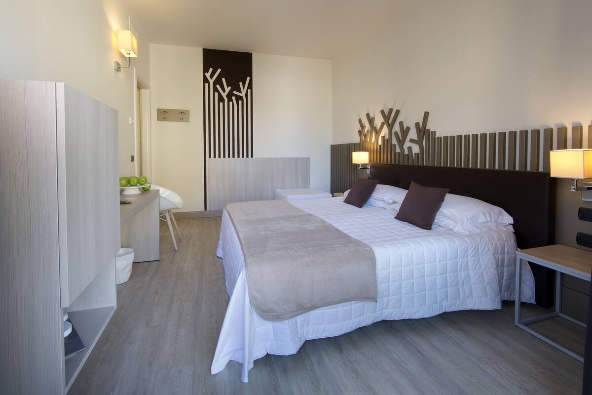 Une chambre d’hôtel moderne avec un grand lit, des tables de chevet, un bureau et un miroir.