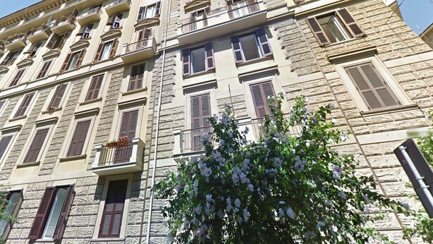 Un immeuble à plusieurs étages, doté d’une façade en pierre, de nombreux balcons et de fenêtres avec volets.