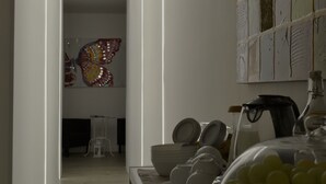 Une cuisine moderne avec un luminaire, une œuvre d’art représentant un papillon et une vitrine en verre contenant des objets jaunes.