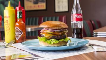 A burger on a plate with condiments and a Coca-Cola bottle on a table.