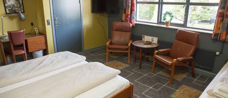 A hotel room with a bed, two chairs, a small table, a TV, and a window with curtains.