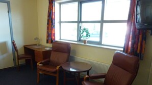 A room with two brown leather chairs, a small wooden table, a desk with a computer, and a window with curtains. - Wittrup Motel (Albertslund)
