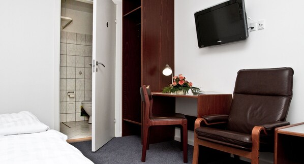 Habitación de hotel con cama, escritorio con silla, televisor y zona de ducha.