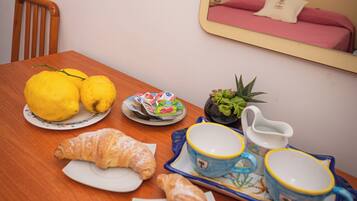 Una mesa de desayuno con limones, un croissant, un plato de pasteles, una planta pequeña y un espejo que refleja una cama.