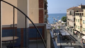 Ein Balkon mit Meerblick, eine Straße mit Geschäften und ein Gebäude mit einer roten Backsteinsäule.
