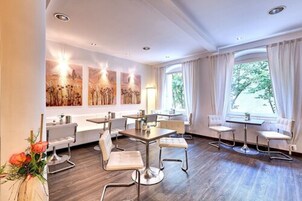 Una habitación de hotel moderna con un ventanal grande, un área de comedor con mesa y sillas, y obras de arte en las paredes.