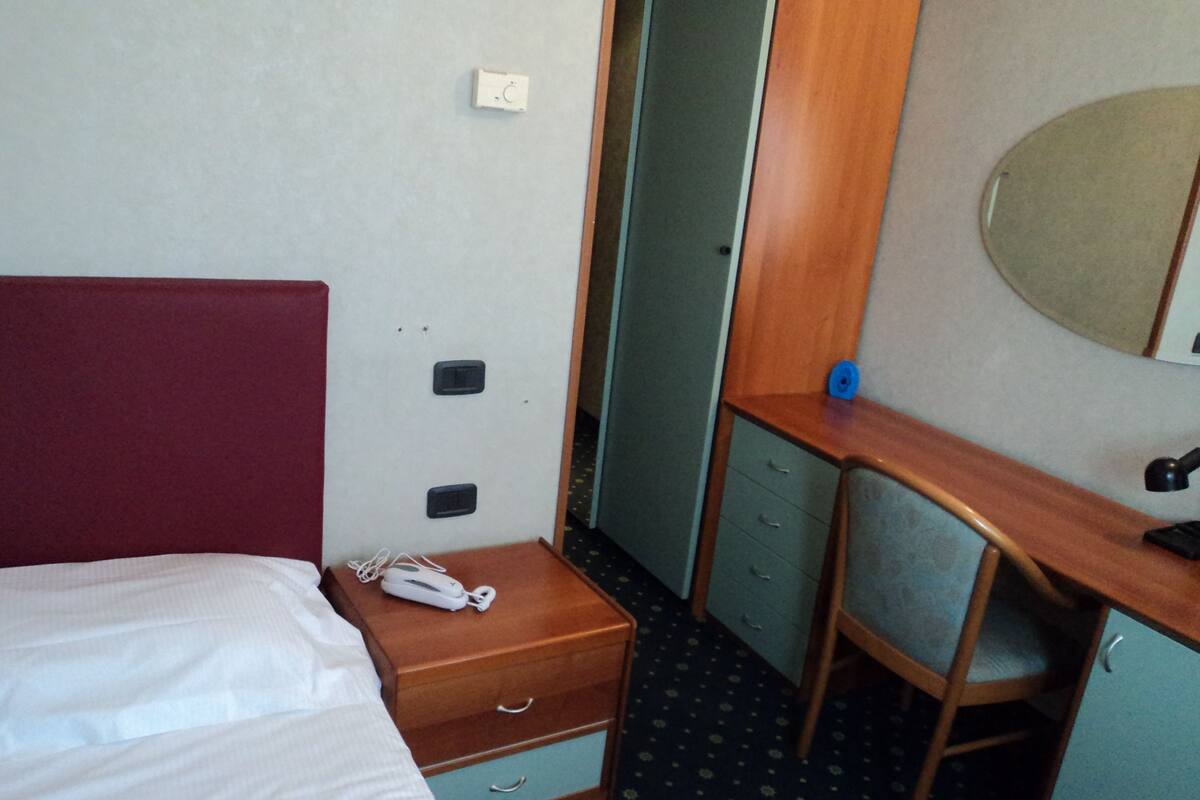 Une chambre d’hôtel comprenant un lit, un bureau avec une chaise, un miroir et un petit tiroir.
