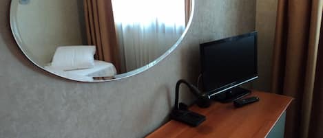 A hotel room with a wooden desk, a television, a mirror, and a bed with white linens.