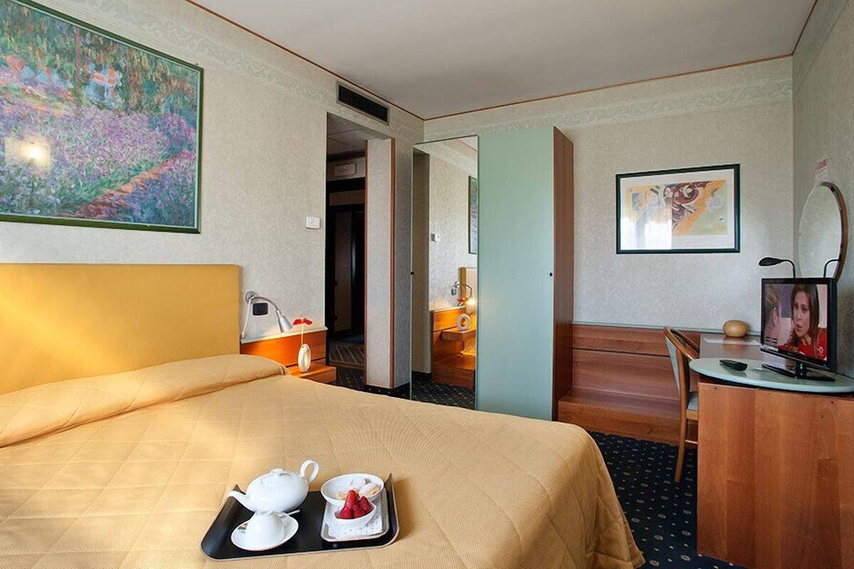 Une chambre d’hôtel avec un lit, un bureau avec une télévision, un tableau au mur et un plateau avec une théière et des tasses.