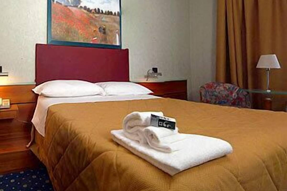 Une chambre d’hôtel avec un lit, un tableau au mur, une table de chevet, une lampe et une chaise.