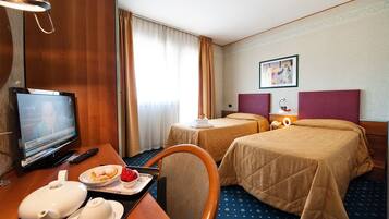 Une chambre d’hôtel avec deux lits, une télévision, un bureau avec une théière et une assiette de nourriture, et un tableau accroché au mur.