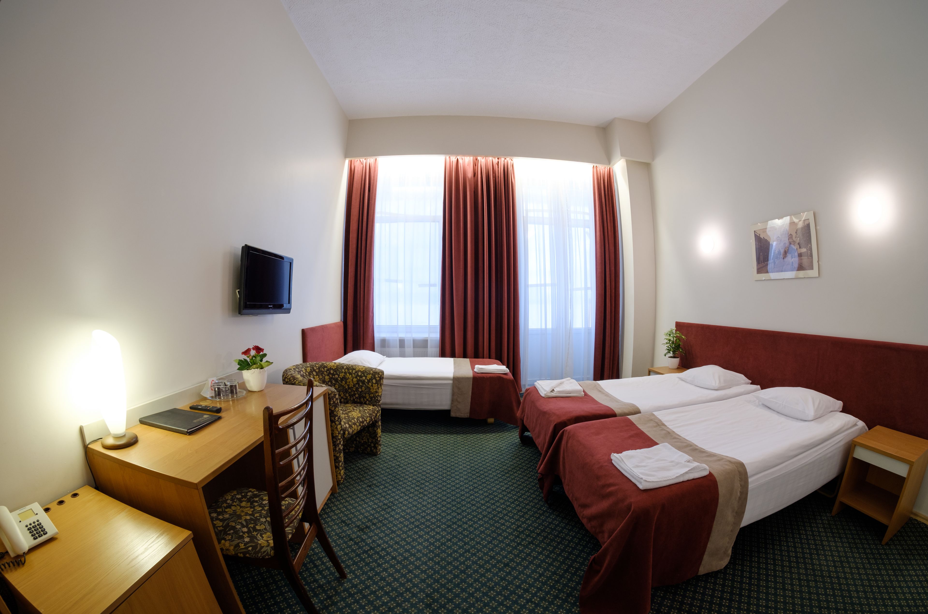 Une chambre d’hôtel avec deux lits, un bureau avec une lampe, une chaise, une télévision et une fenêtre avec des rideaux.