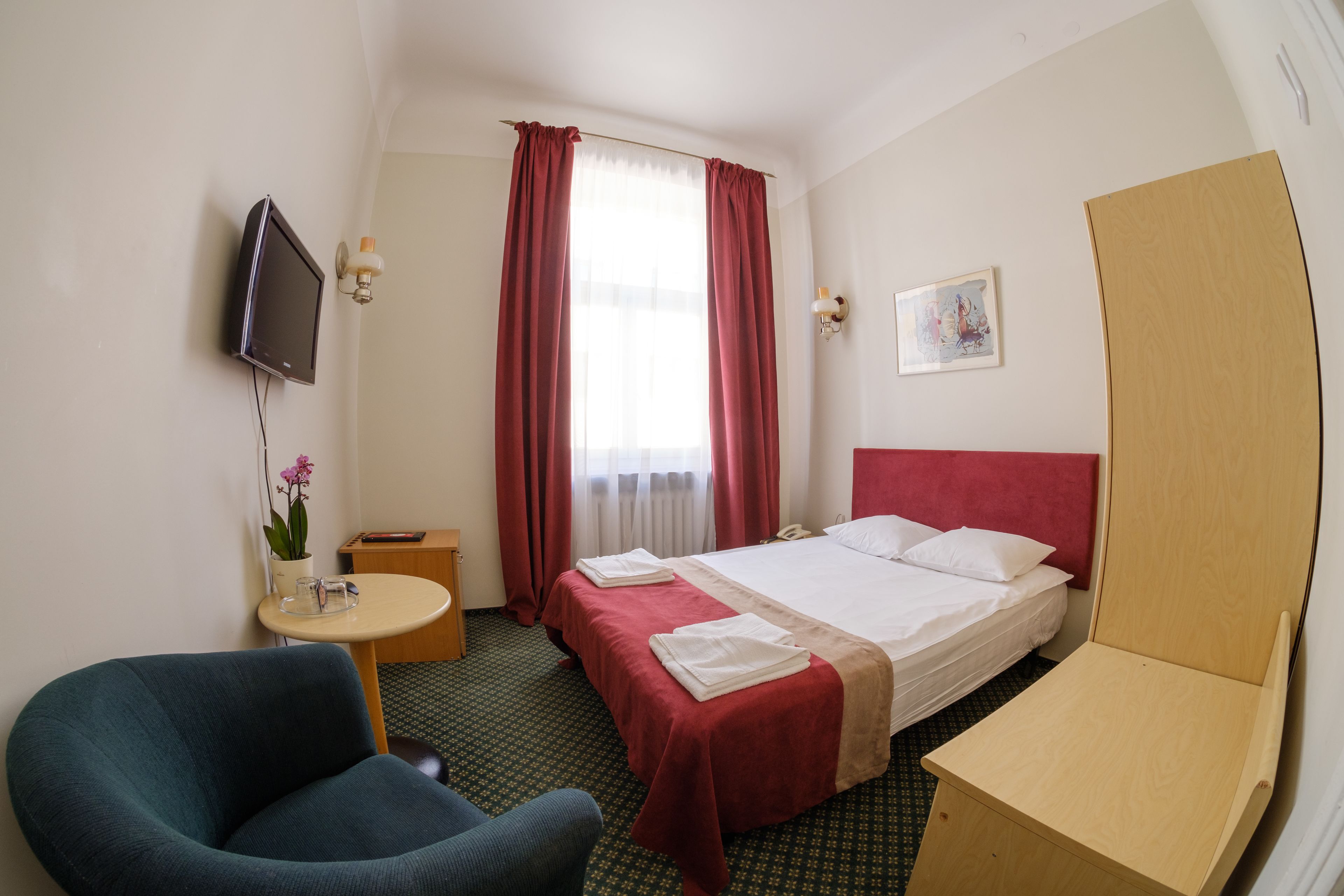 A hotel room with a bed, a desk, a chair, a TV, and a window with curtains.