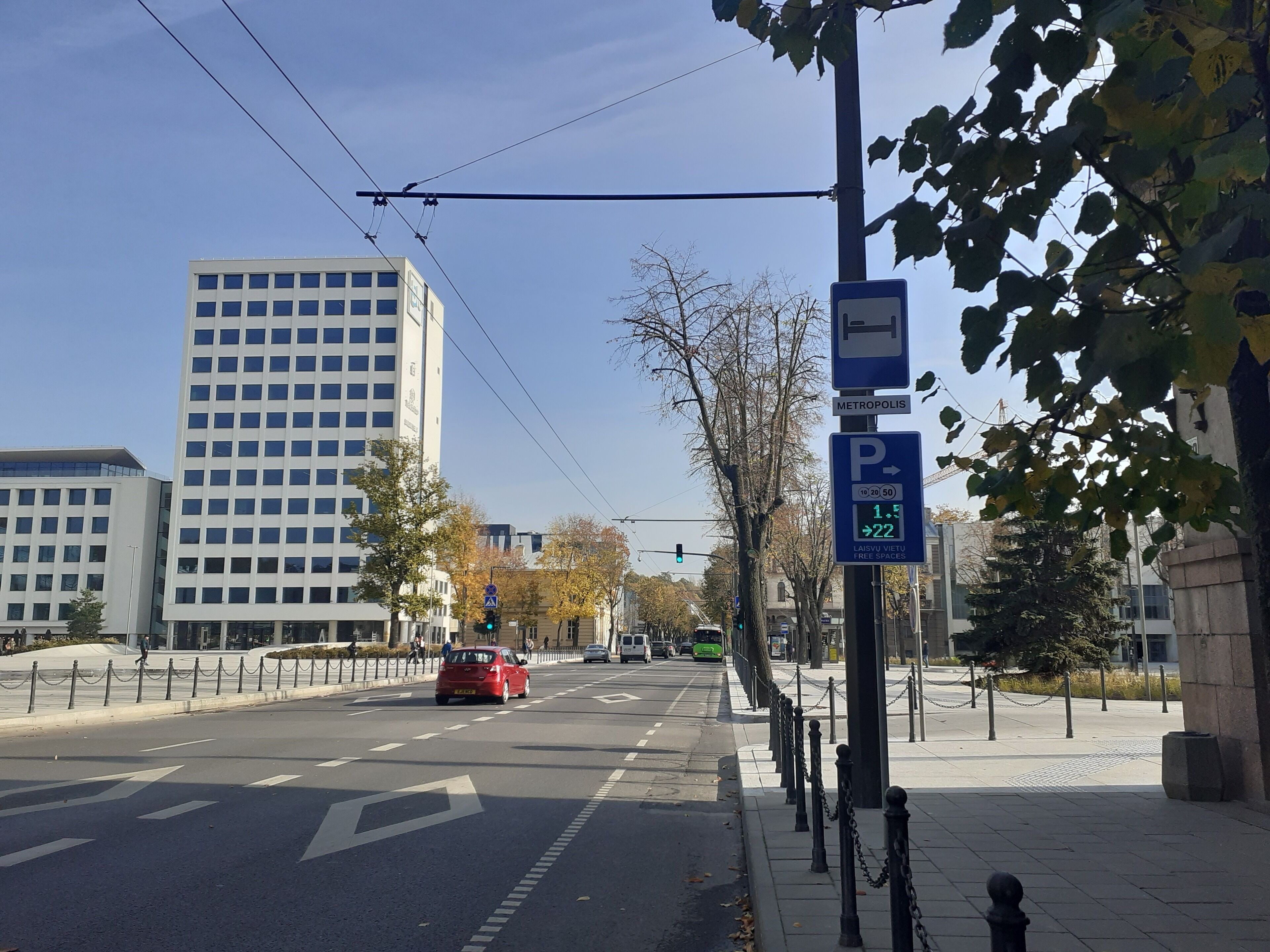 A city street with a parking sign, a tram line, and modern buildings.