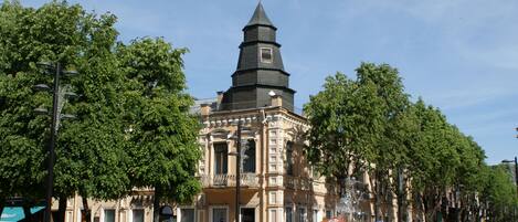 Un edificio histórico con una torre destacada, rodeado de árboles y una fuente.