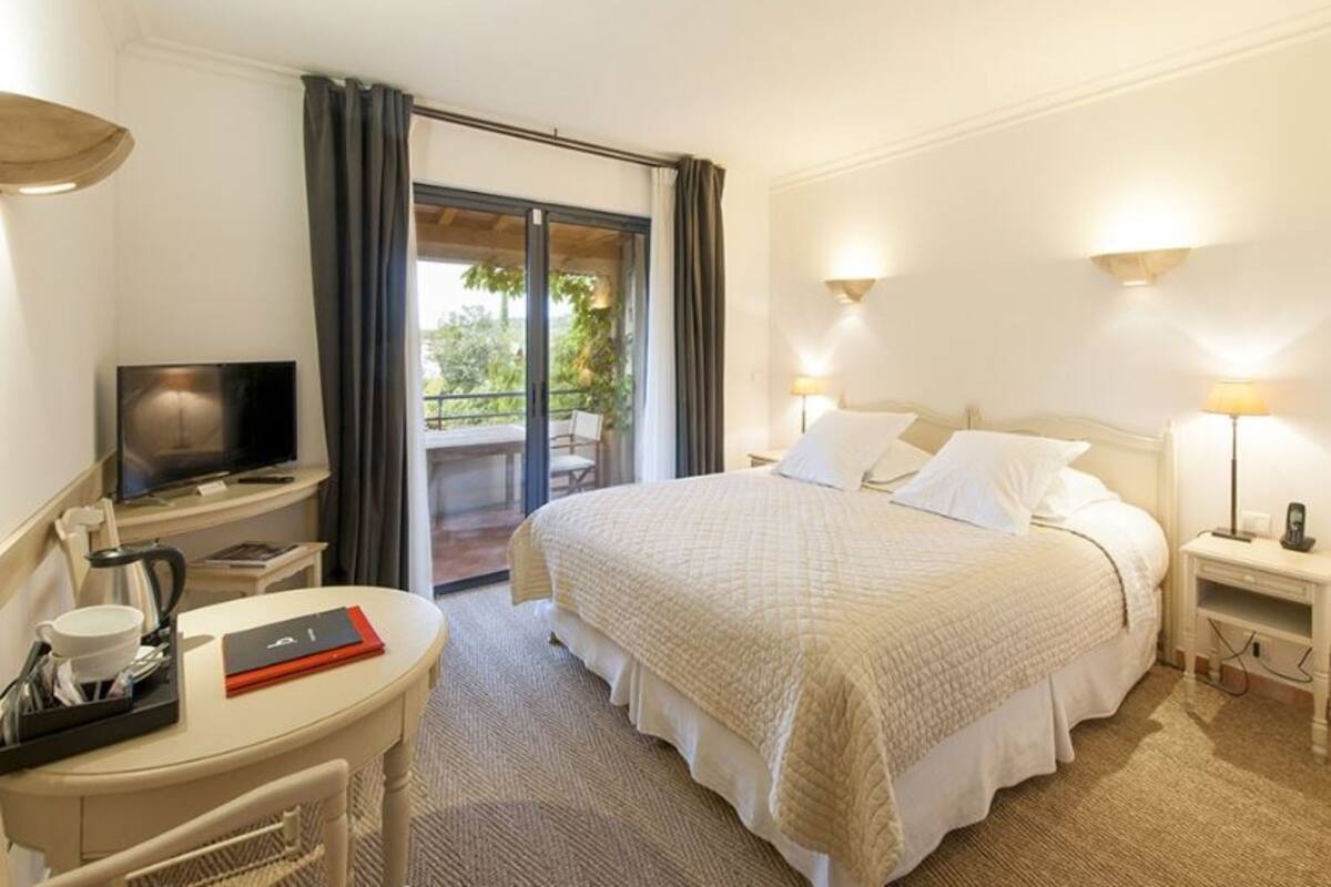 A hotel room with a bed, a desk with a television, a coffee maker, and a view of the outdoors.