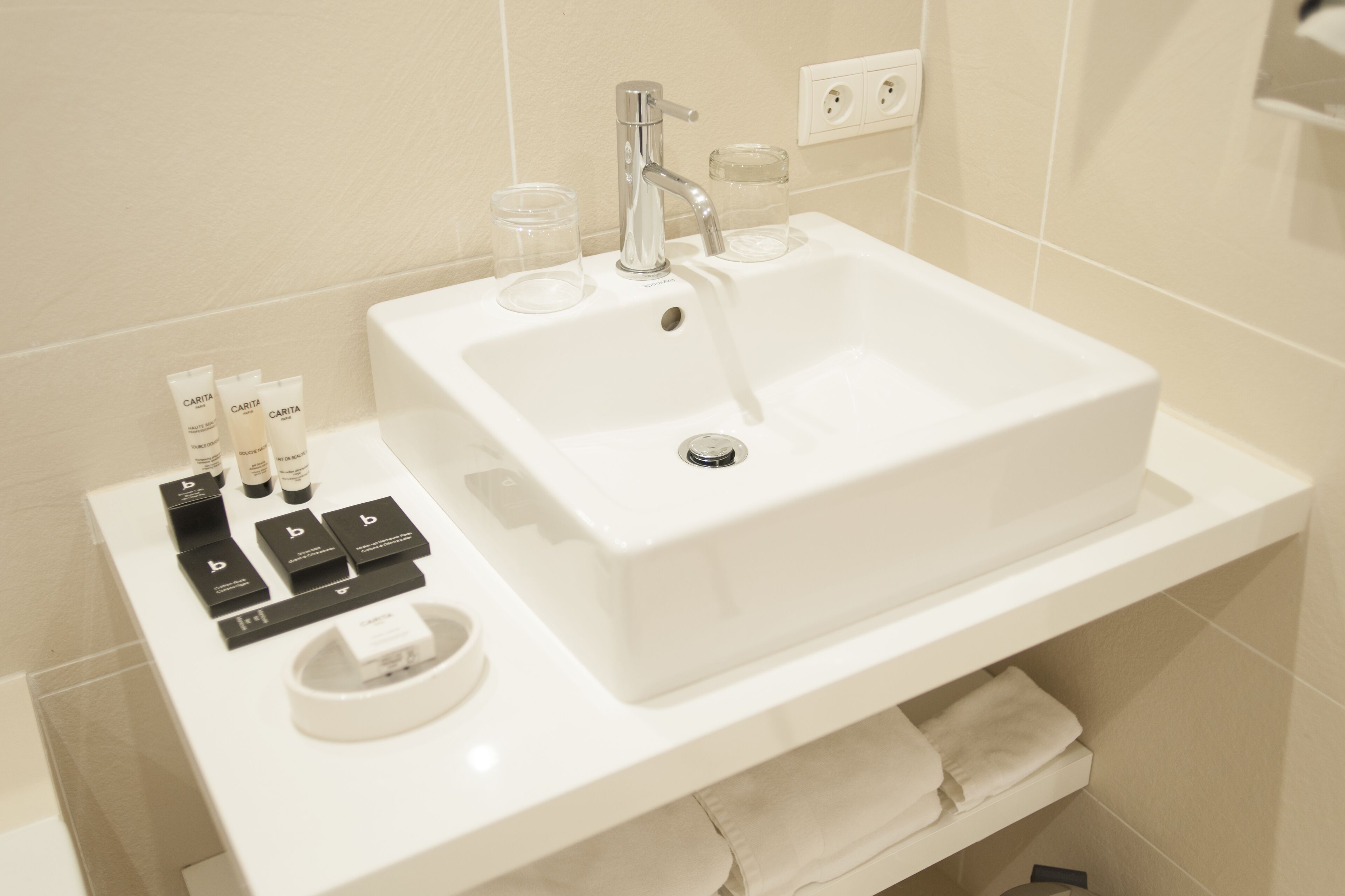 Un baño con lavamanos blanco, un espejo y artículos de aseo en un estante.