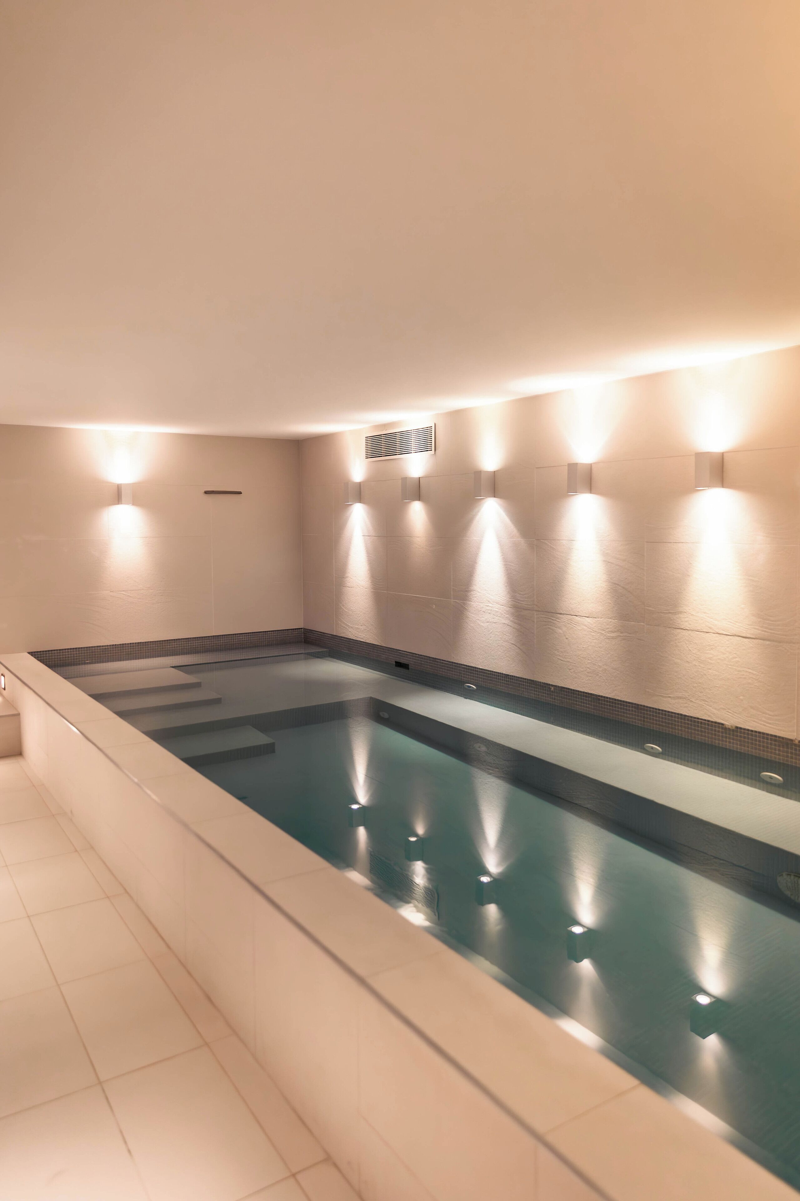 En swimmingpool med kakel på golv och väggar, omgiven av ett område med ljusfärgat kakel.