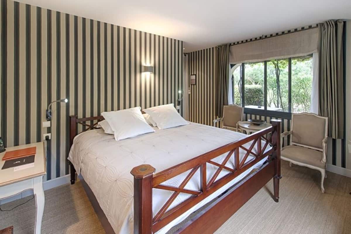 A hotel room with a large bed, a desk, a chair, and a window with curtains.