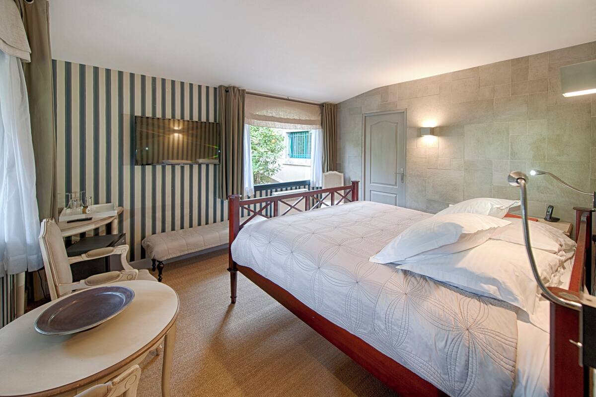A hotel room with a bed, a desk, a chair, a small table, and a balcony with a view.