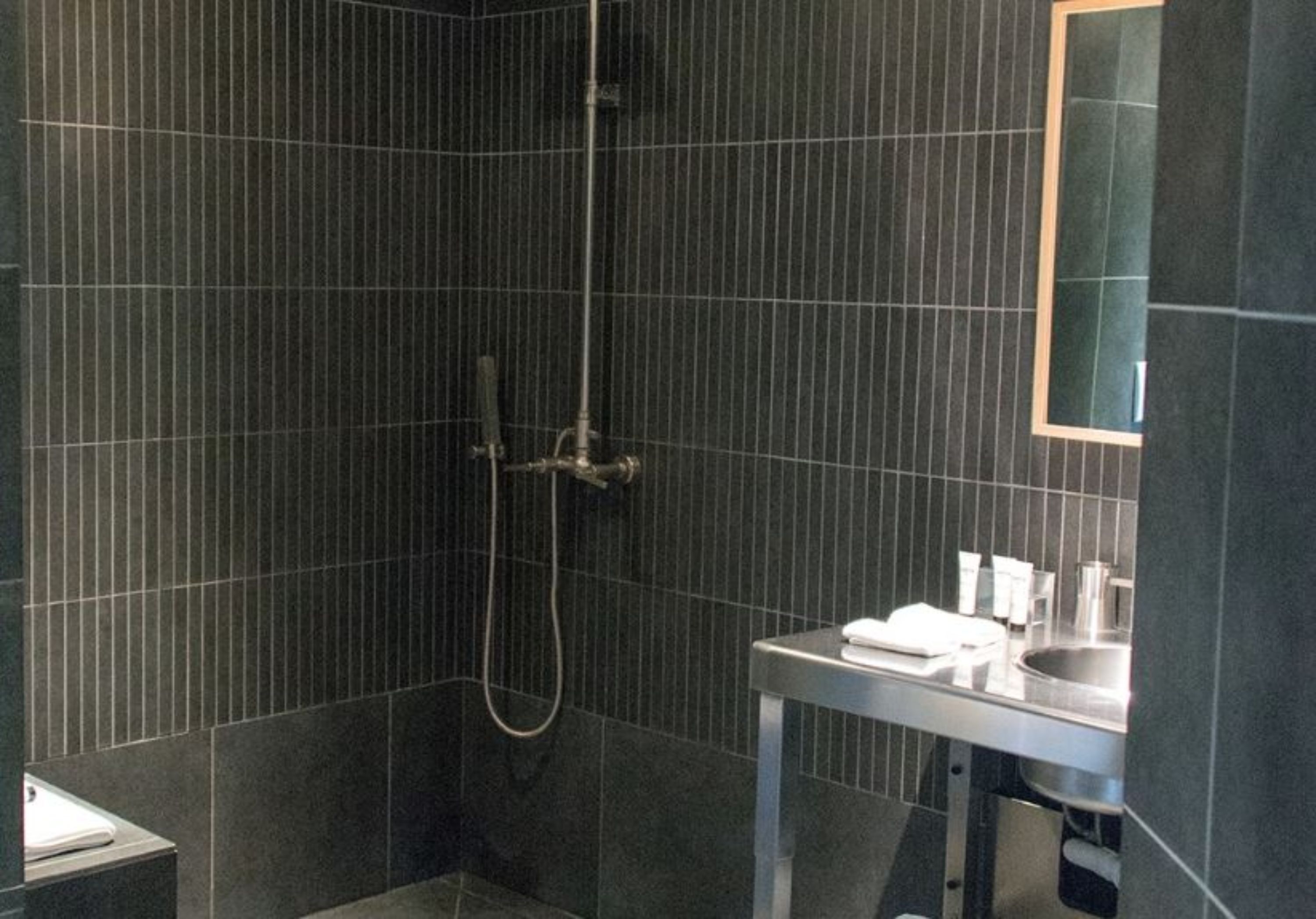 A modern bathroom with dark tiled walls, a shower area, and a vanity with a mirror.
