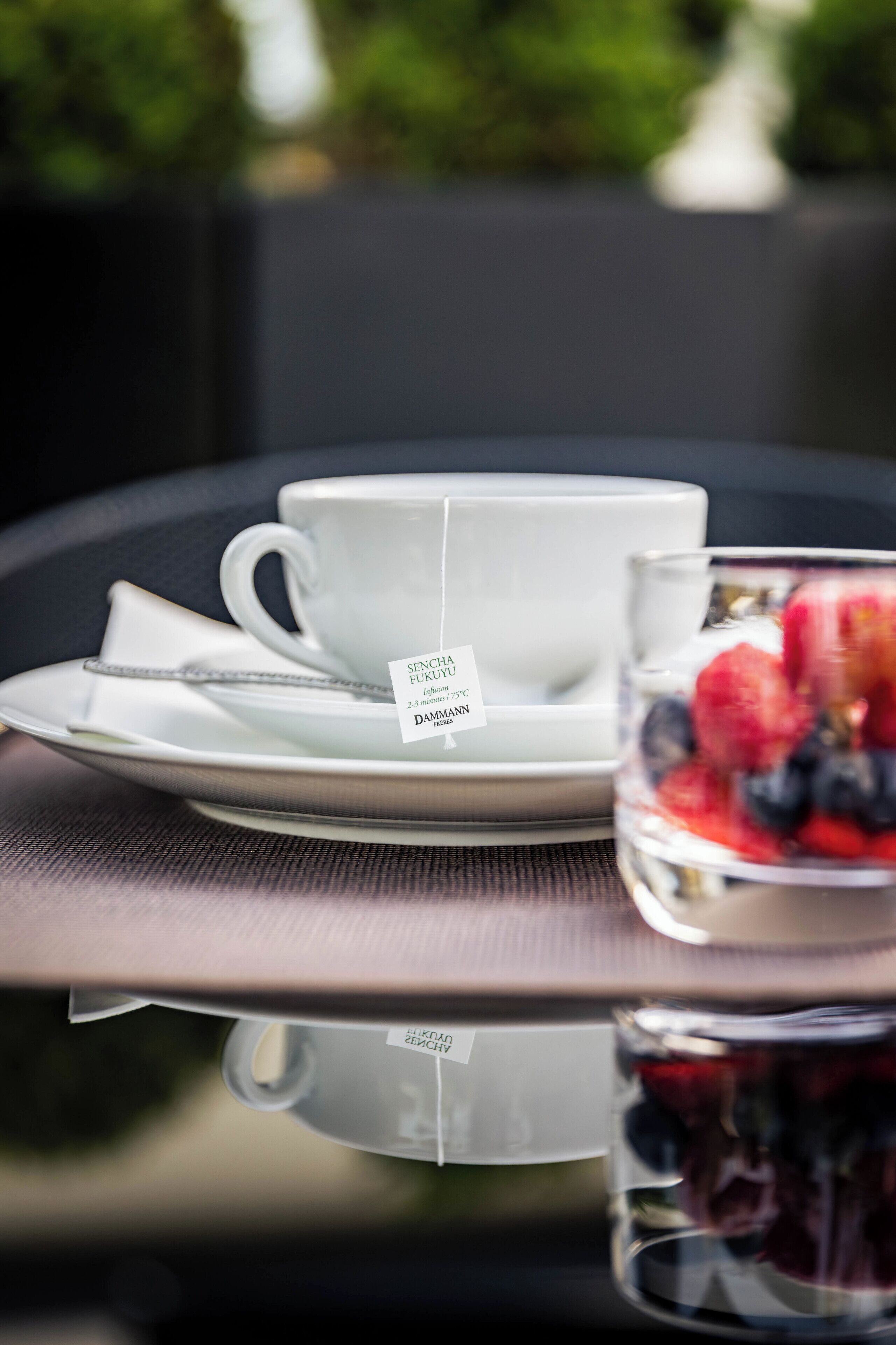 A table with a white cup and saucer, a glass of berries, and a teabag labeled "SENCHA FUKUYA."