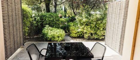 A patio with a black table and chairs, surrounded by a garden with various plants and trees.