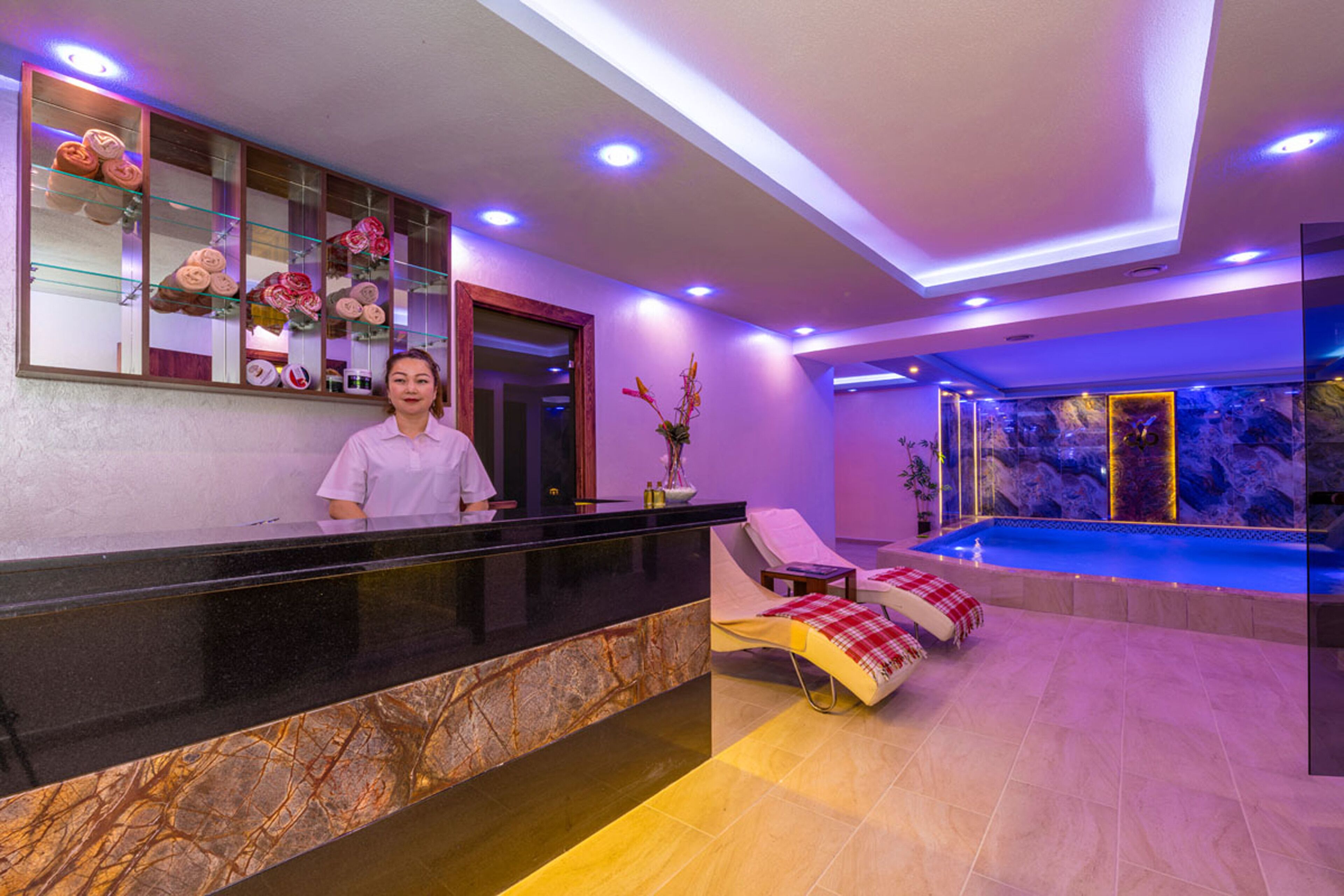 A reception area with a marble counter, a reception desk, a lounge chair, and a pool area with a view of the pool.