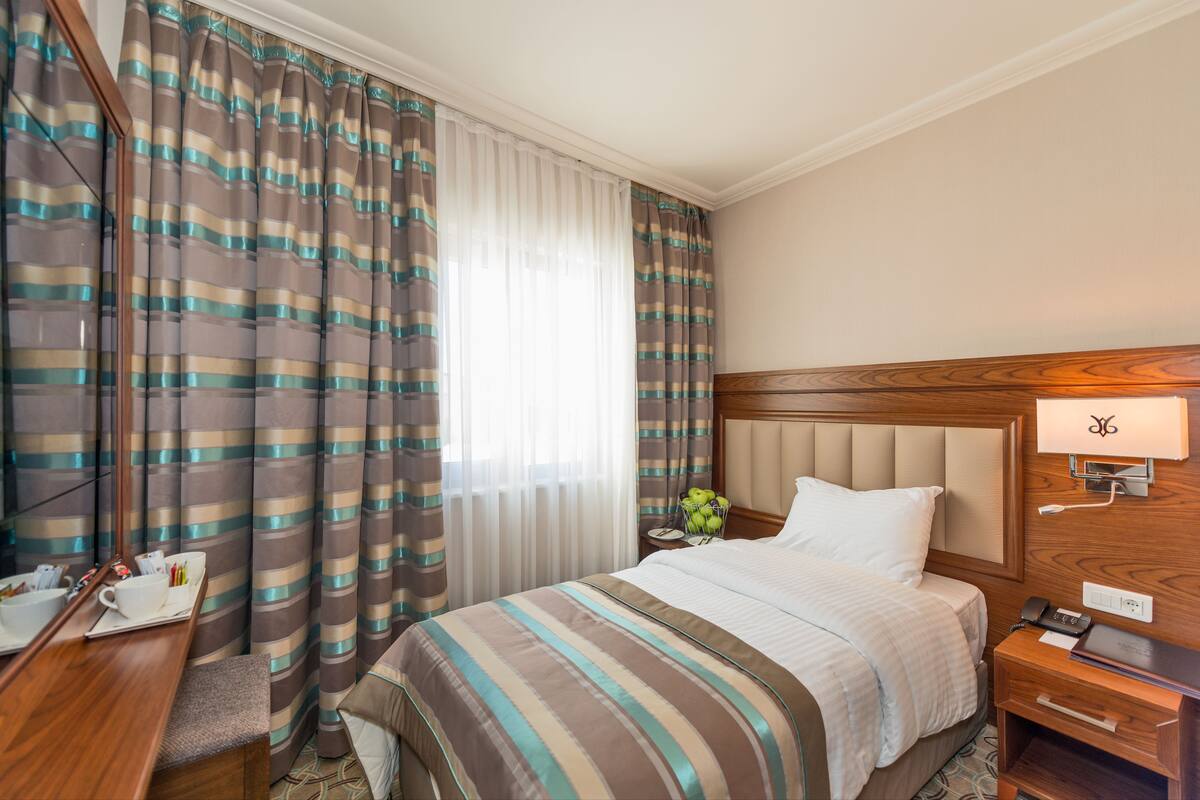 A hotel room with a bed, bedside table, lamp, and curtains.