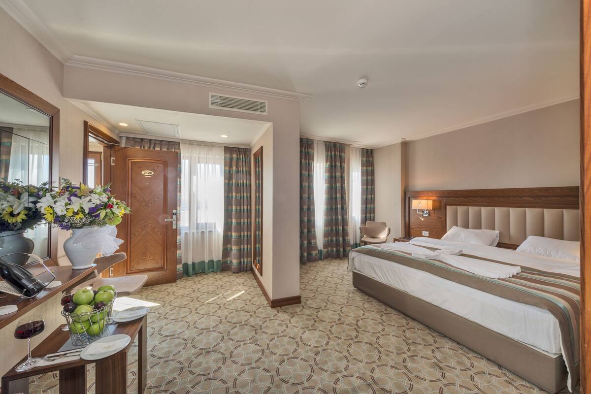 A hotel room with a large bed, a desk with a telephone and a vase of flowers, and a bathroom door.