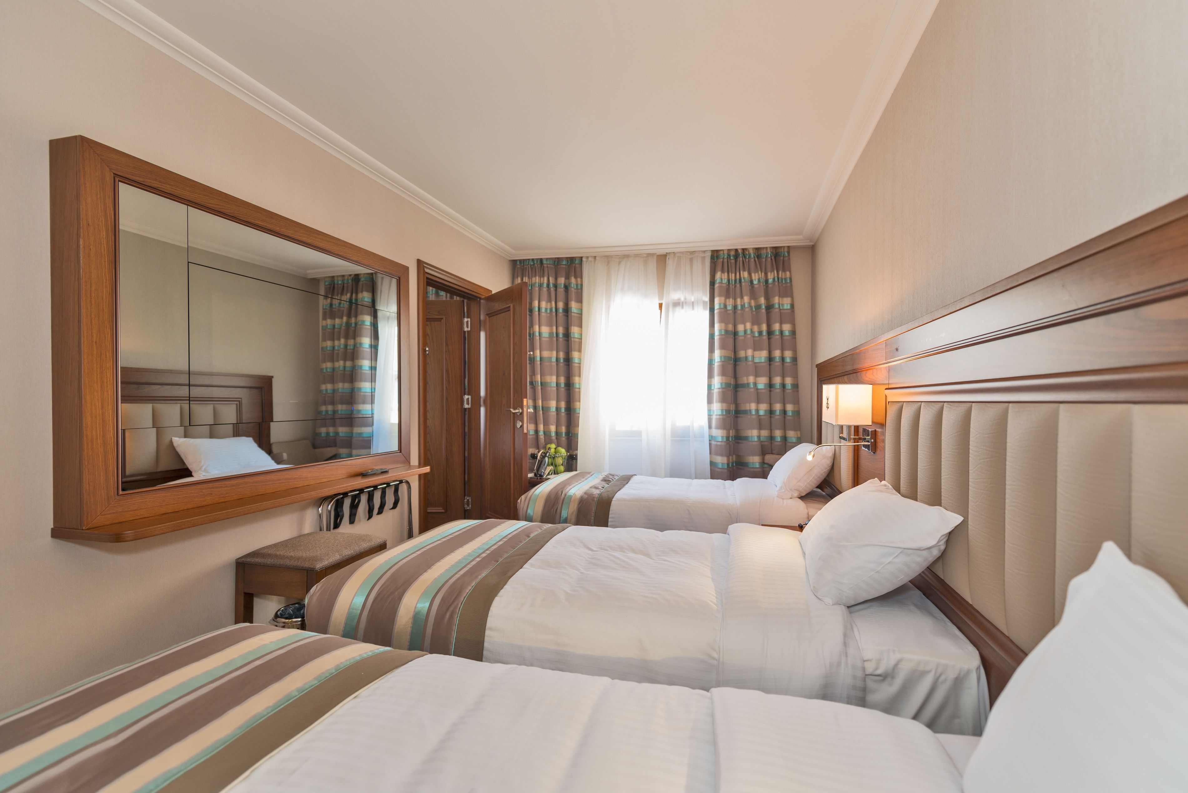 Habitación de hotel con dos camas, un espejo grande, una mesita de noche y una ventana con cortinas.