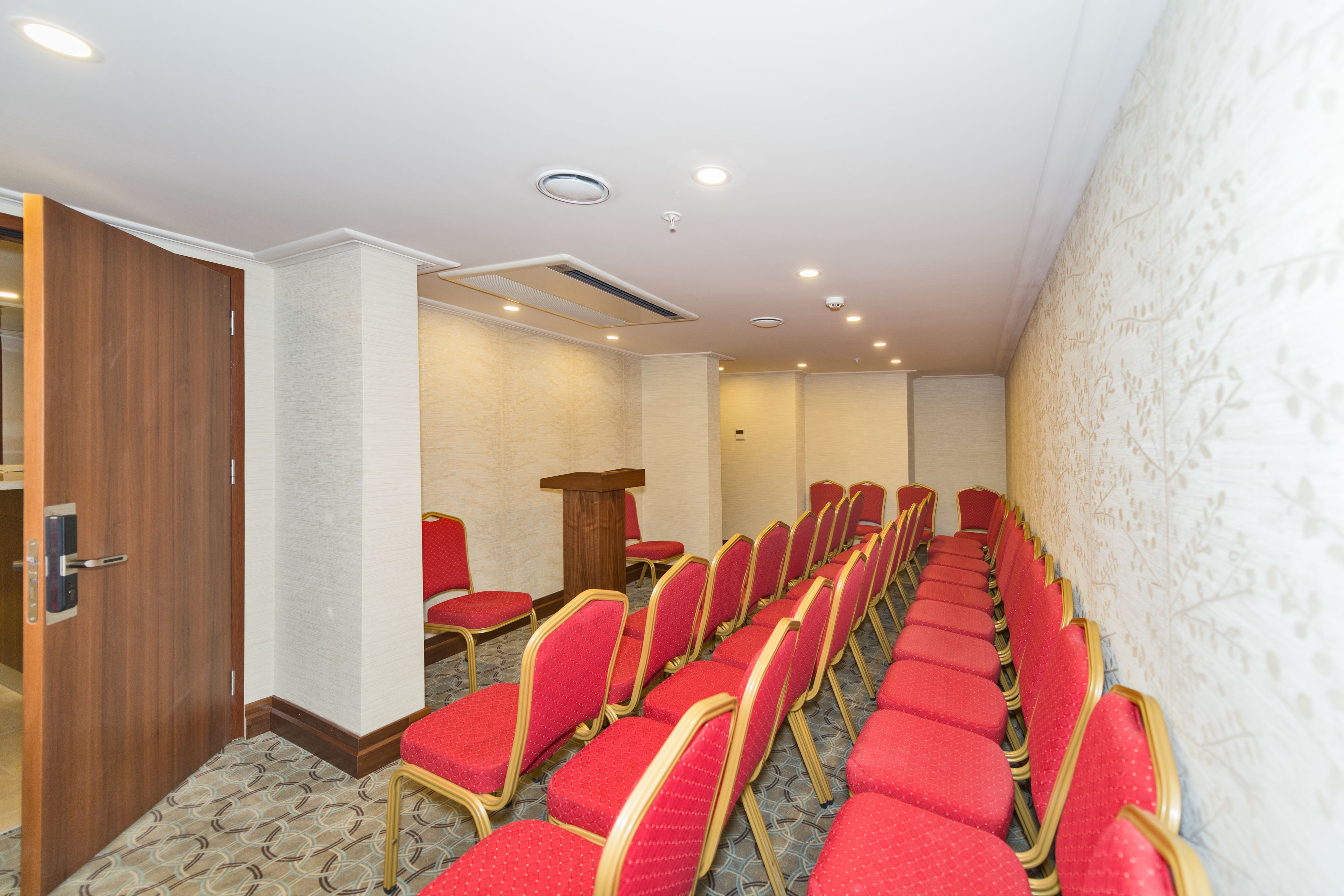 A conference room with rows of red chairs, a wooden door, and a podium.