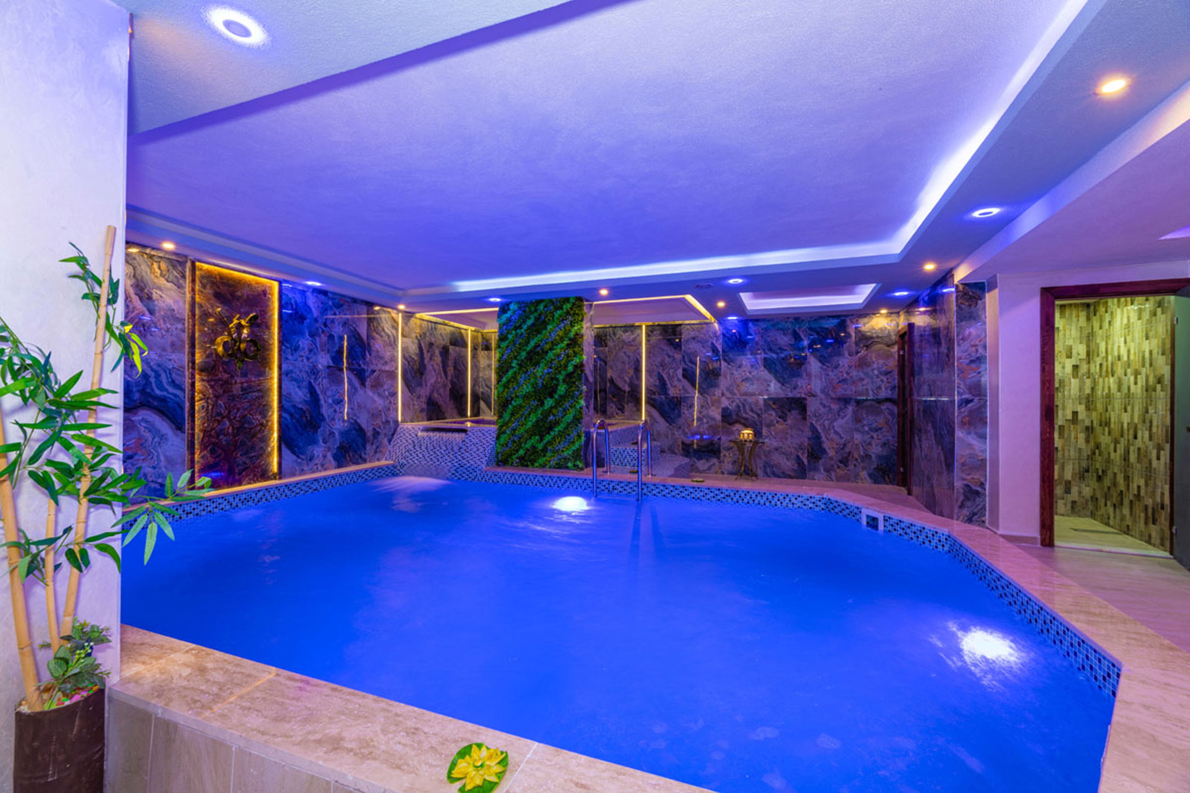 Una piscina interior moderna con un elemento acuático azul, rodeada de paredes de mármol e iluminación ambiental.